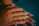 Hands with long, manicured nails displaying various nail art designs including rhinestones and glitter. The nails have a glossy finish, with some featuring sparkly turquoise and others clear with embellishments. The skin tone is warm and contrasts with the blue background.