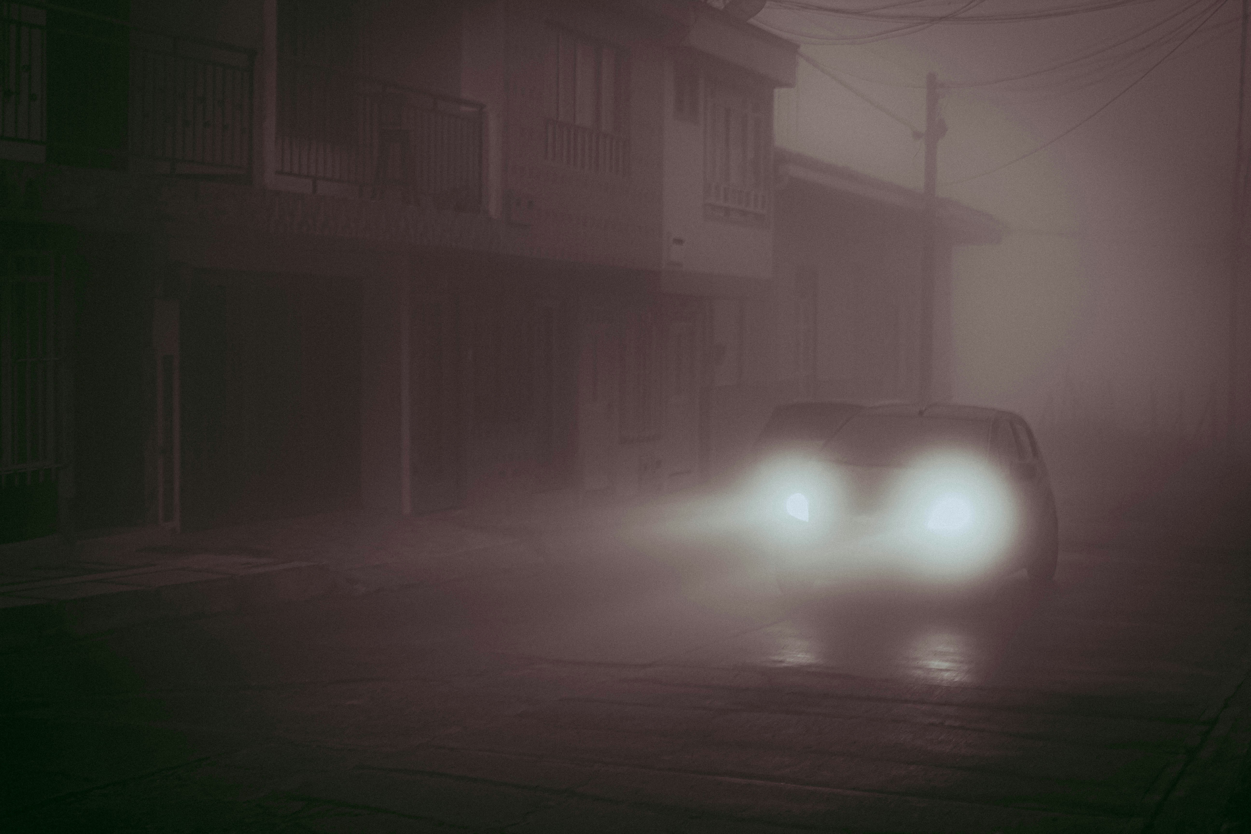 Security patrol vehicle driving at night, urban street, bright headlights, dark moody atmosphere