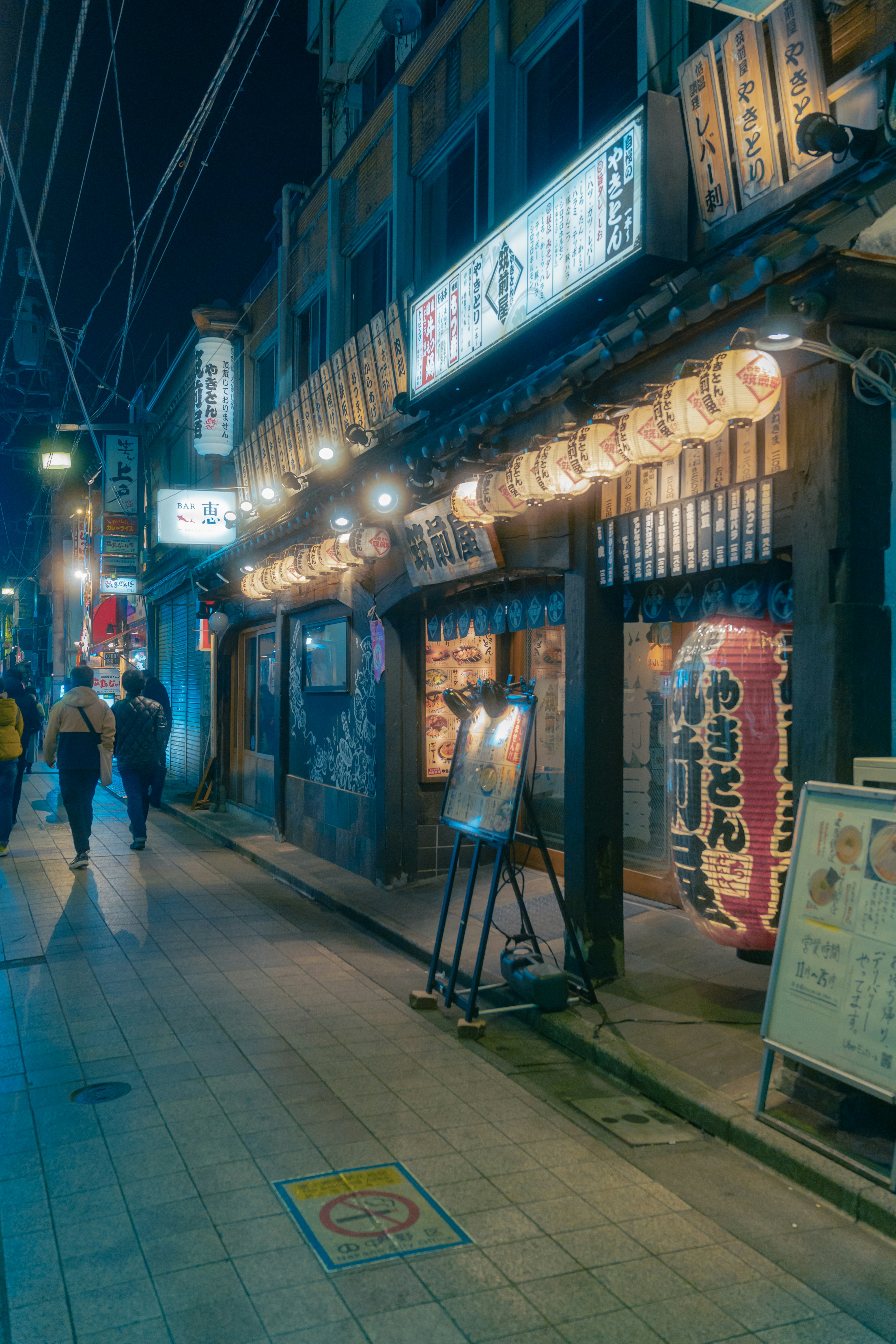 a city street at night with people walking on the sidewalk
