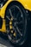 Close-up view of a sleek, black car tire with intricate alloy wheel design, set against a vibrant yellow car body. The surface of the tire appears glossy and well-maintained, with lighting highlighting the modern wheel structure.