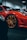 A close-up view of a luxurious red sports car with gold rims, parked indoors. The sleek body design and glossy finish emphasize its high-end nature.