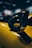 A close-up shot of a car's side mirror with a glossy, carbon fiber design and the letters 'P1' in yellow. The background features soft-focus shapes, enhancing the emphasis on the sleek and stylish component.