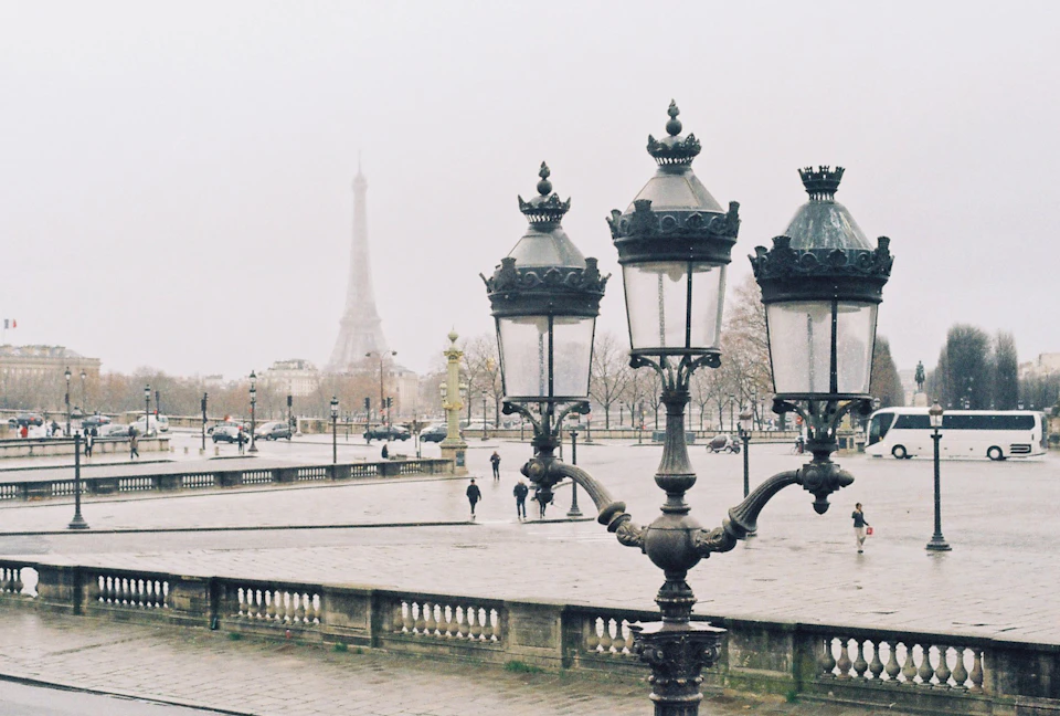 Ornate triple street lamps on the balustrade of Place de la Concorde on a grey, misty day, the Eiffel Tower faint in the background above bare trees