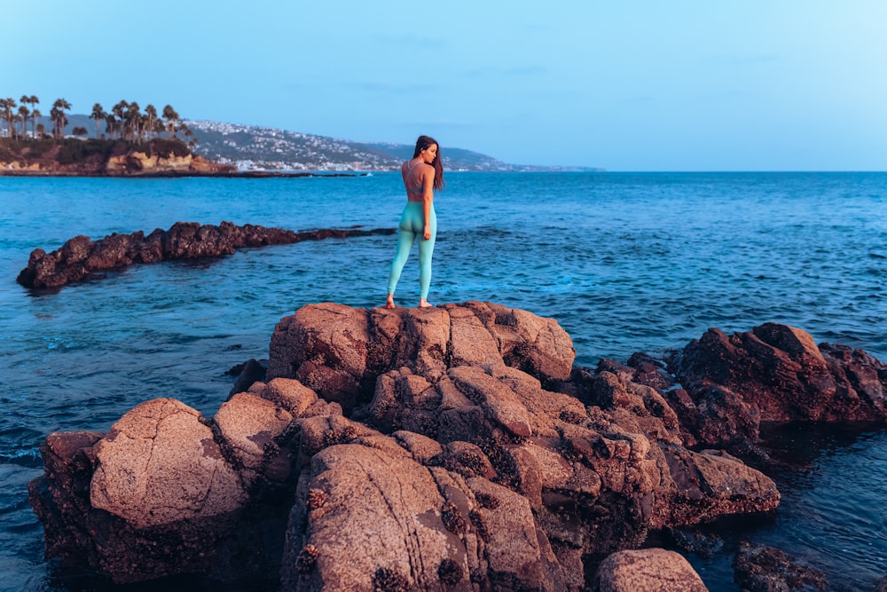 a woman standing on rocks in the ocean
