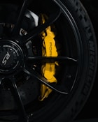 Close-up shot of a high-performance car wheel featuring a yellow brake caliper with the brand name Porsche written on it. The tire is a Michelin with a clear tread pattern visible. The wheel hub displays the RS logo.