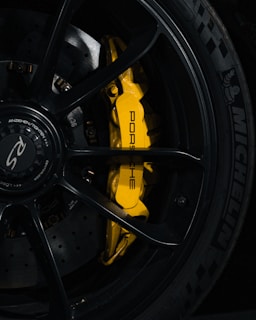 Close-up shot of a high-performance car wheel featuring a yellow brake caliper with the brand name Porsche written on it. The tire is a Michelin with a clear tread pattern visible. The wheel hub displays the RS logo.