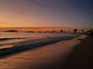 a sunset view of a beach with a city in the background