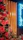 A vibrant floral arrangement with large, lush red and pink roses is set against a backdrop of vertical wooden panels. A neon sign in bright blue spells out 'Bloom' on the right, adding a modern touch to the scene.