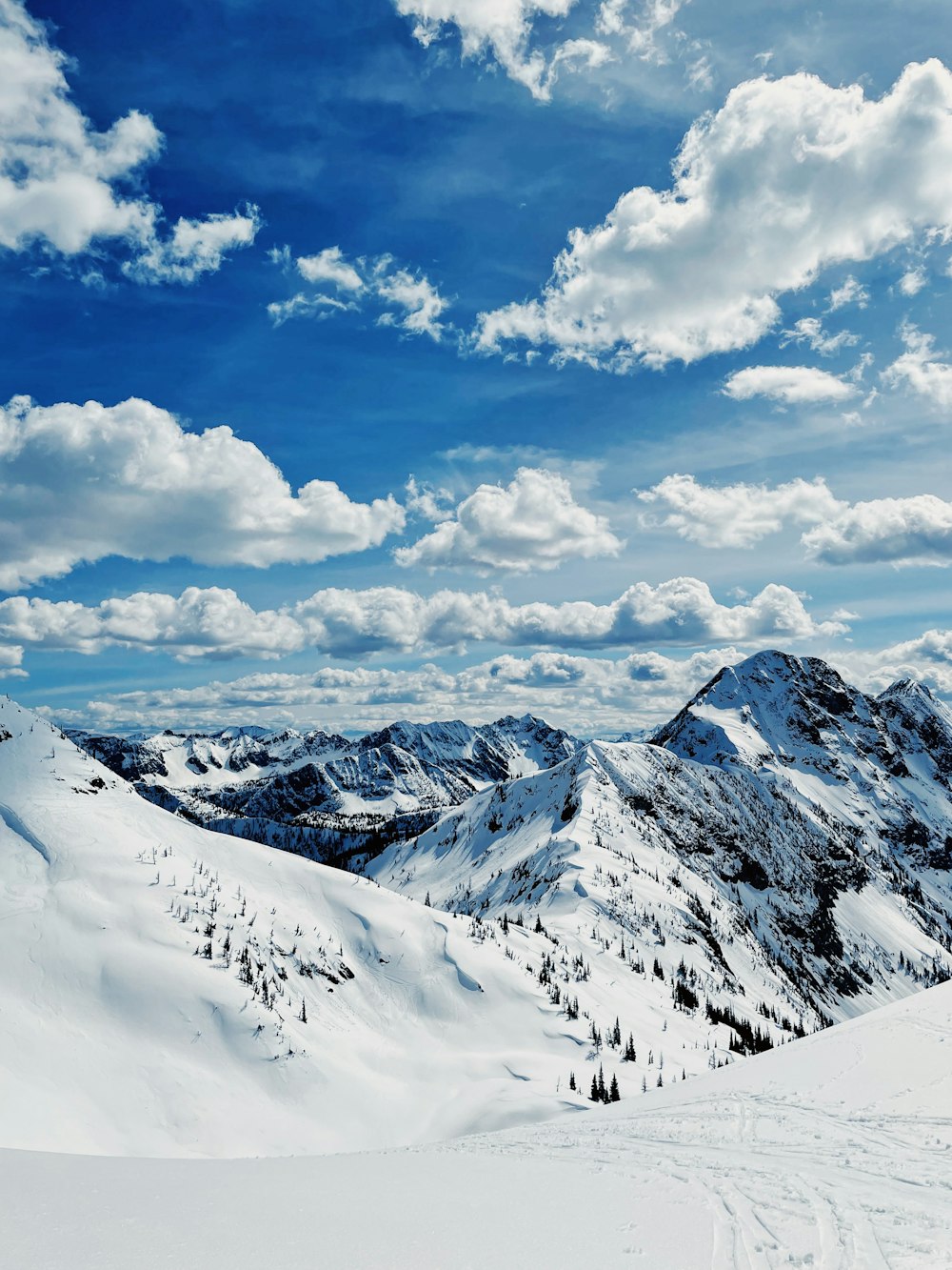 a view of a snowy mountain range under a cloudy blue sky