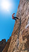 Climber ascending a steep limestone cliff under a bright blue sky.