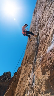 A climber confidently leading a route with a belayer focused below on a bright day.