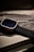 A smartwatch with a rugged black band rests atop its packaging. The watch face is dark, and the box beneath displays the product branding in a sleek, modern font. The overall aesthetic is minimalist and high-tech.
