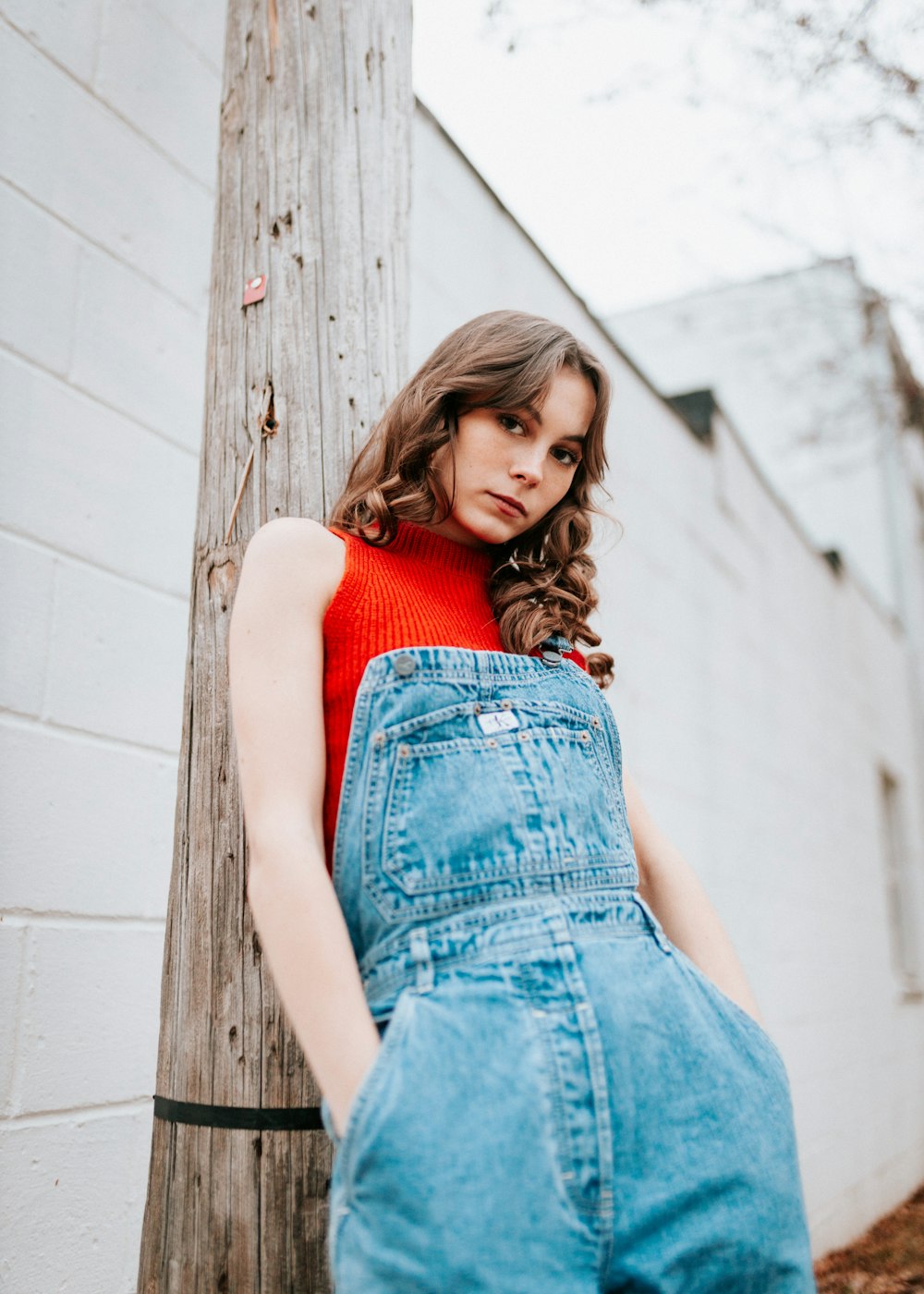 a woman in overalls leaning against a wooden pole