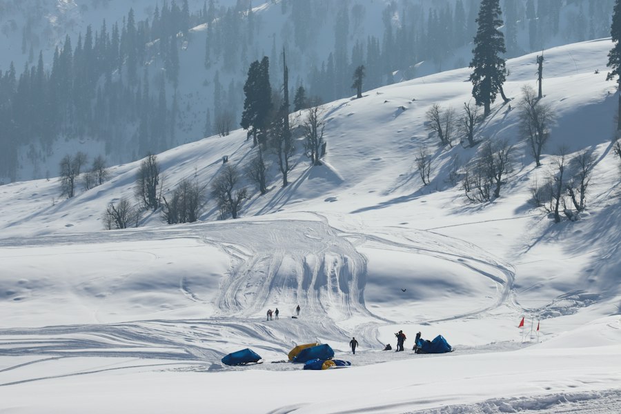 Snow-covered slope with pine trees and a few people and tents in Gulmarg, Kashmir
