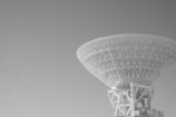 A large radio telescope with a complex, lattice structure dominates the scene. The background is a clear sky, creating a stark contrast with the intricate design of the telescope.