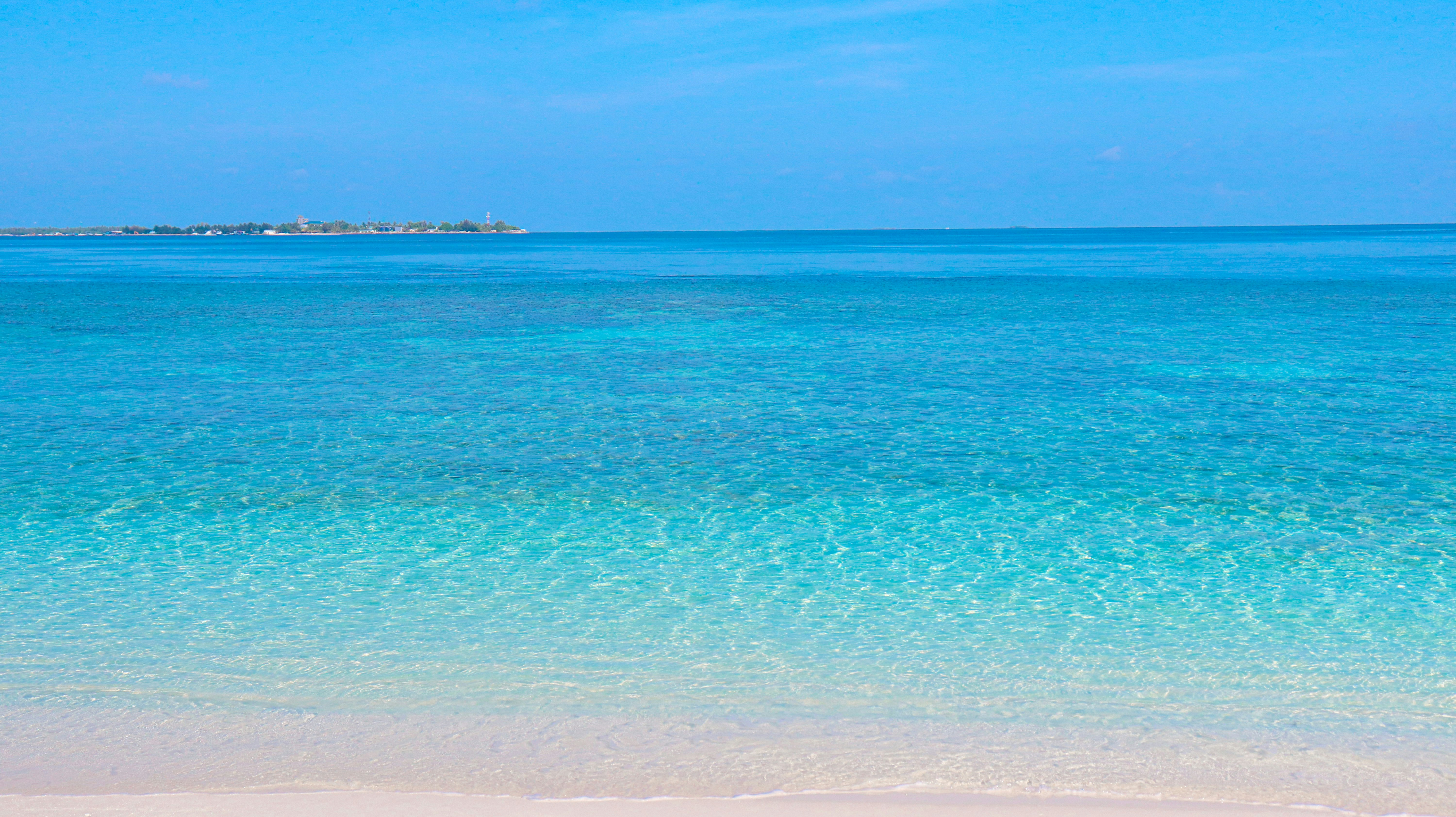 a beach with clear blue water and a boat in the distance