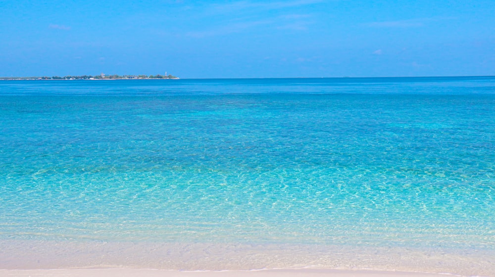 a beach with clear blue water and a boat in the distance