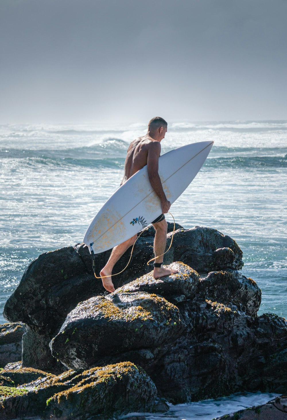a man carrying a surfboard on top of a rocky beach