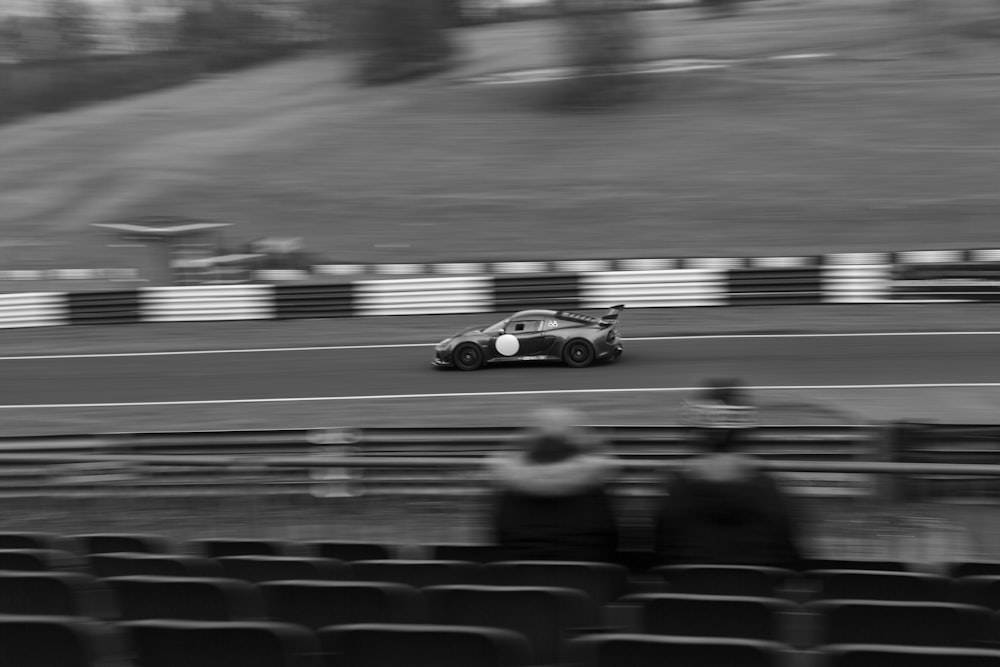 a black and white photo of a car driving on a race track