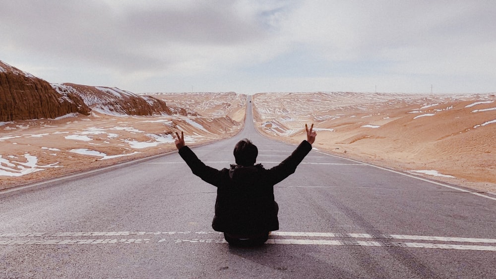 a person sitting on the side of a road with their arms in the air