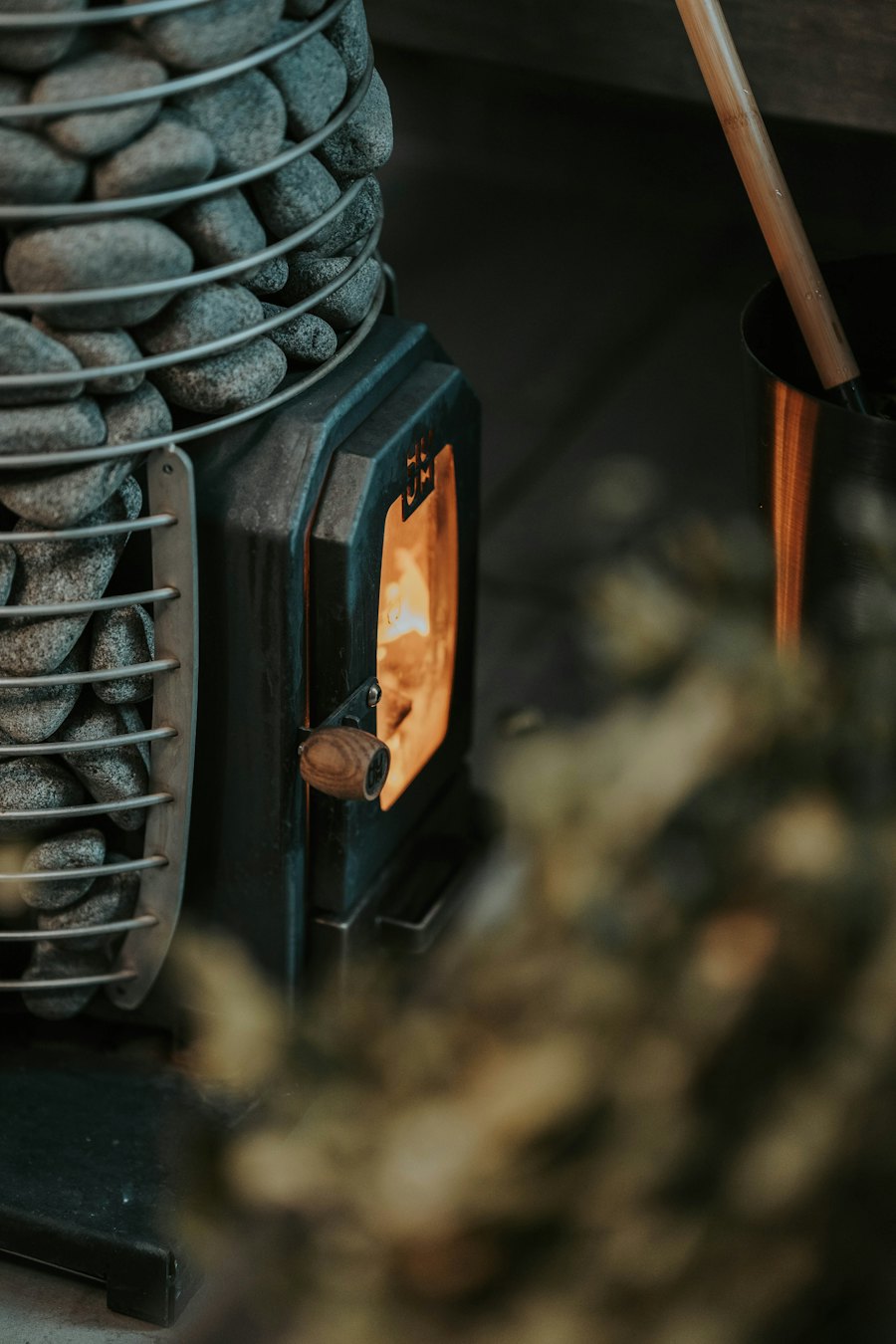 Fire burning behind the glass door of a wood sauna stove, with sauna stones stacked above it and a ladle nearby