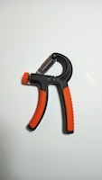 A handheld grip strengthener with black and orange handles is positioned against a plain white background. The design features a spring mechanism at the top, allowing for adjustable resistance.