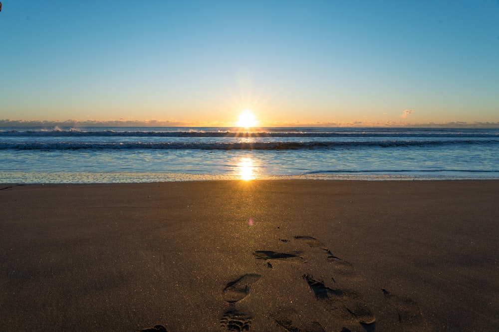 the sun is setting on the beach with footprints in the sand