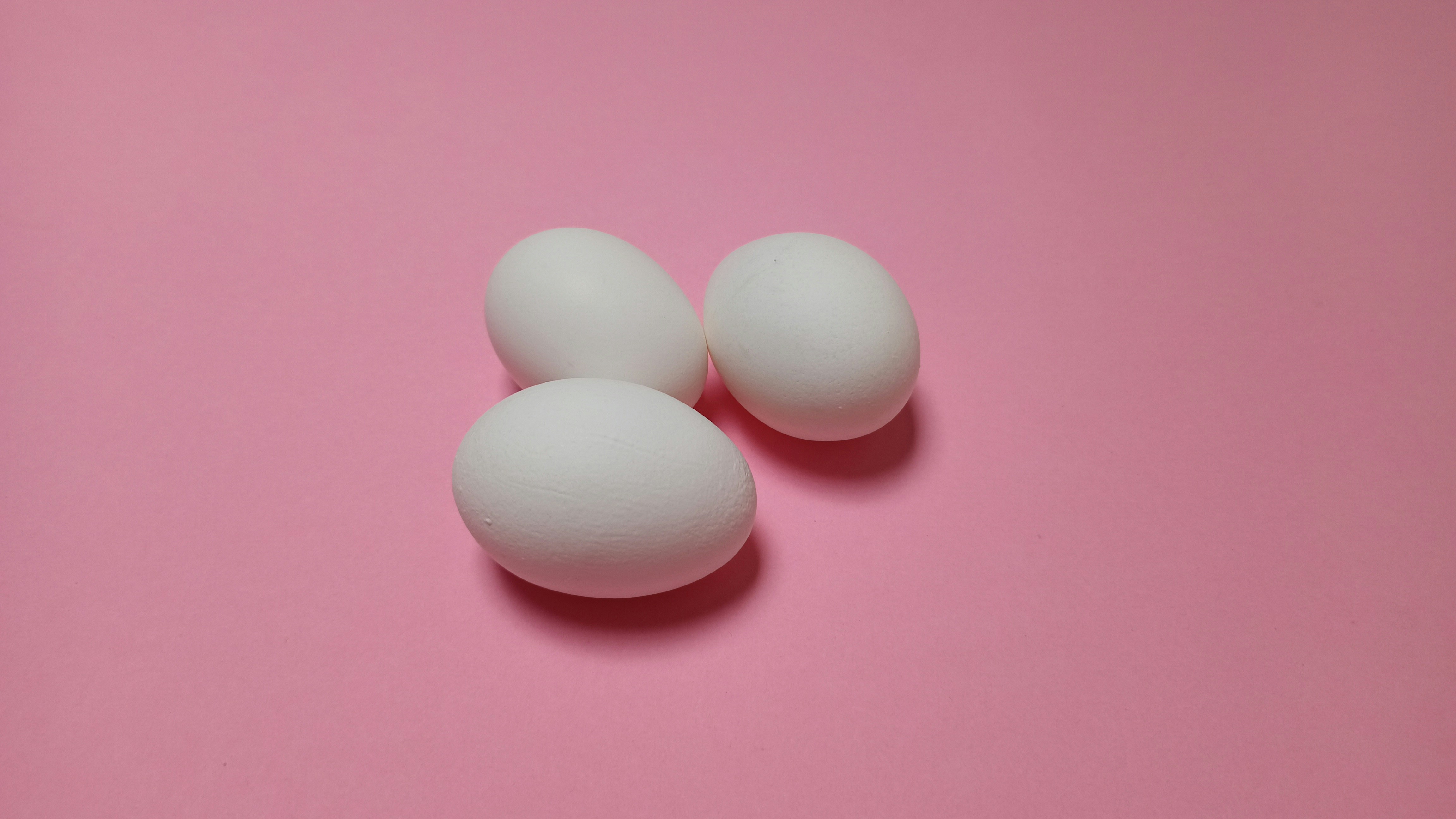three white eggs on a pink background