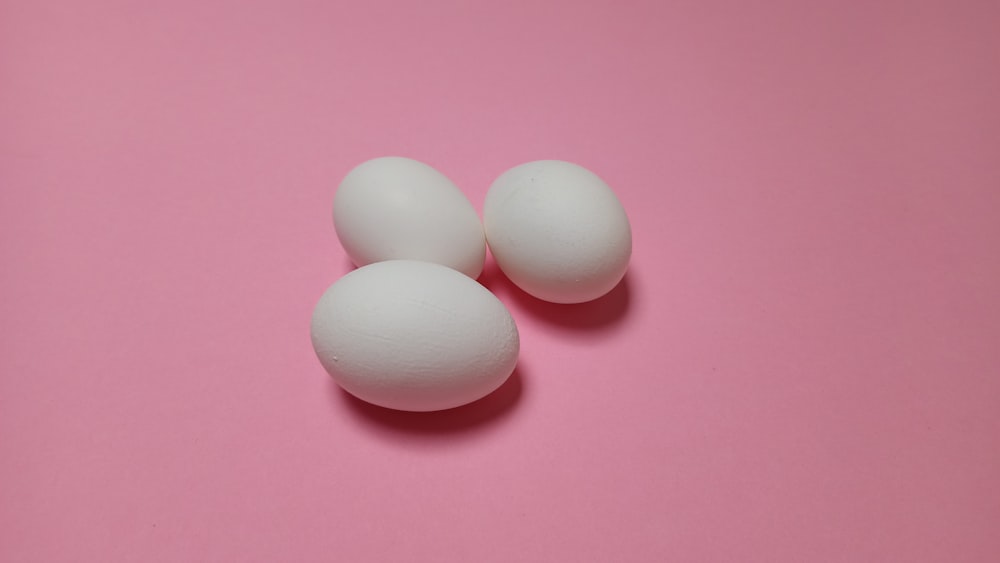 three white eggs on a pink background