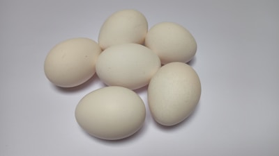 Six light-colored eggs are grouped together on a plain, smooth surface. The arrangement highlights their smooth, oval shapes and their uniform color against the white backdrop.