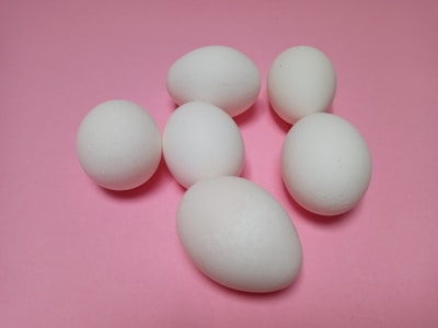 Six white eggs are scattered on a smooth, pastel pink surface. The eggs vary in orientation and are arranged in an informal cluster.