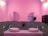 A stylish bathroom features pink walls and a green tiled backsplash. Two round mirrors hang above the sinks, which are placed on a minimalist counter. The sinks have a decorative floral design. Modern light fixtures with spherical bulbs are mounted on the walls, and a soap dispenser and paper towel holder are visible.
