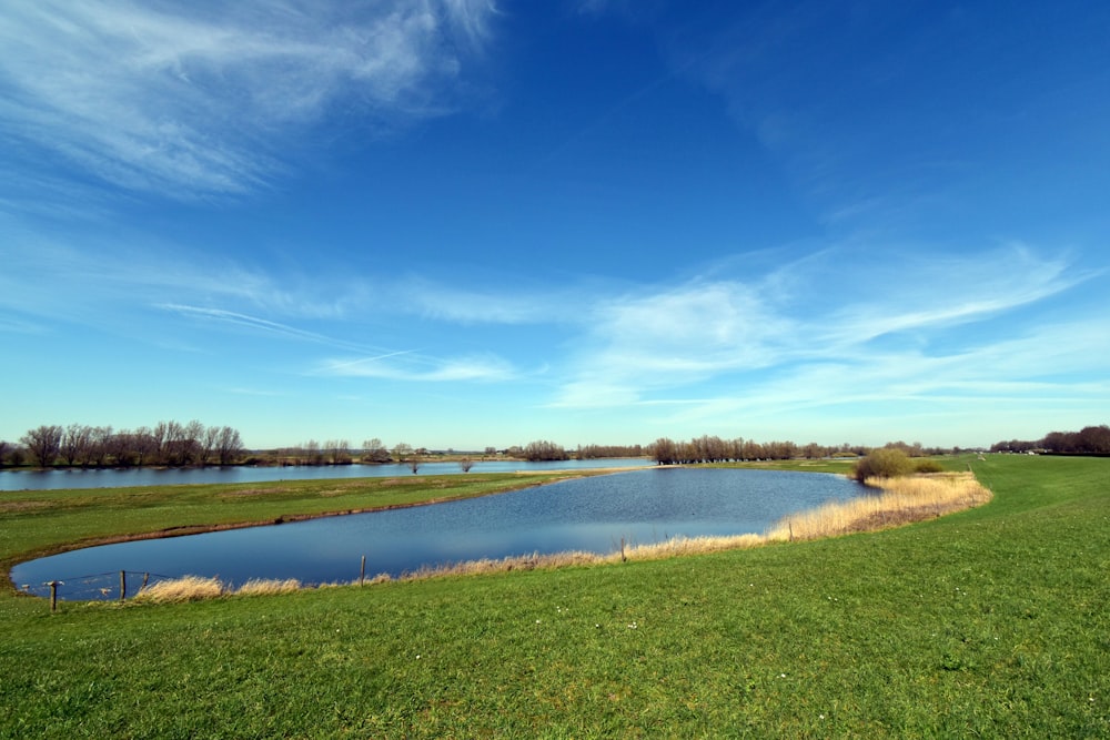 a large body of water surrounded by a lush green field