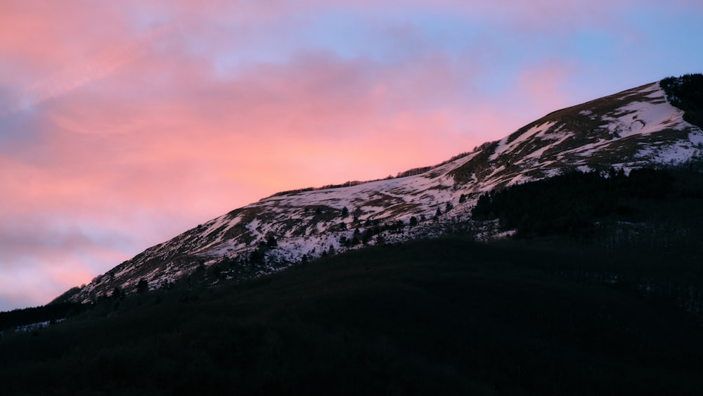 a mountain covered in snow under a pink sky