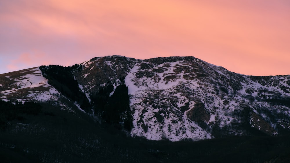 a mountain covered in snow under a pink sky