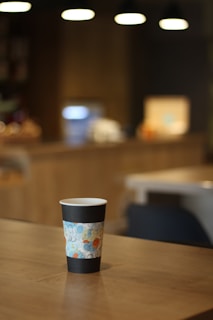 A close-up of a colorful, hand-painted cup resting on a wooden table with soft natural light.