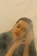 A person with eyes closed and a serene expression, with a hand resting on the side of the face, surrounded by a soft haze that creates a tranquil and dreamy atmosphere.