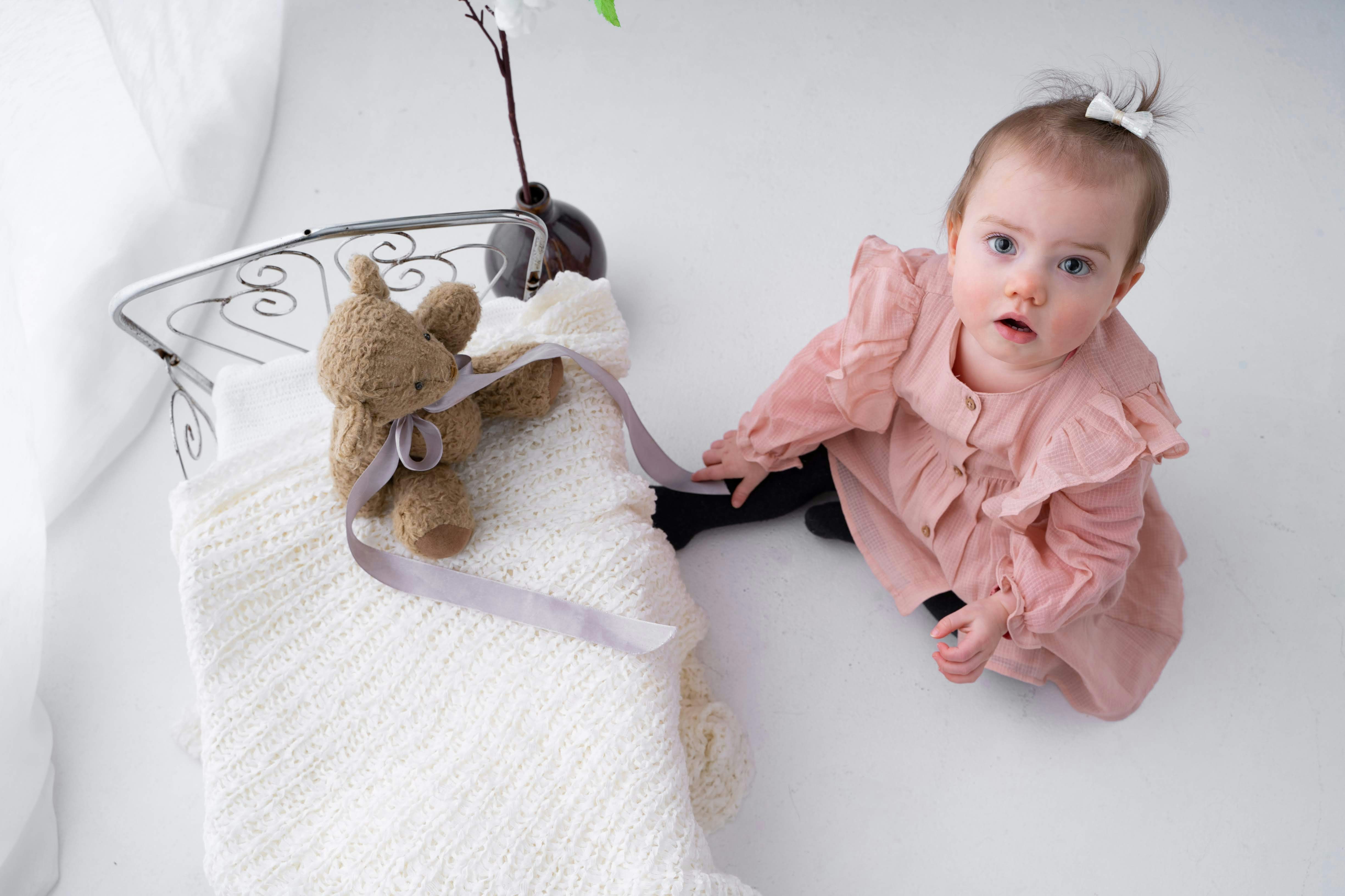 a baby sitting on the floor next to a teddy bear