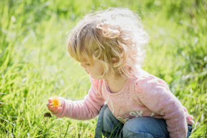 a little girl kneeling in the grass holding a flower