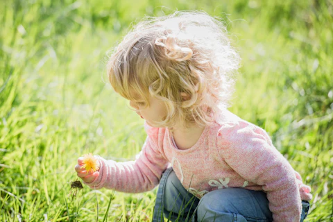 a little girl kneeling in the grass holding a flower