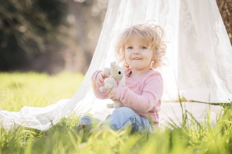 a little girl sitting in the grass with a stuffed animal