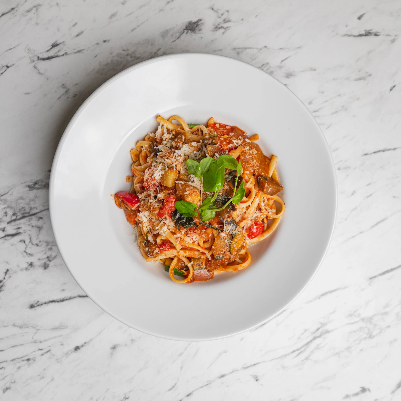A plate of pasta with tomato sauce, basil and shaved cheese, illustrating the sample menu