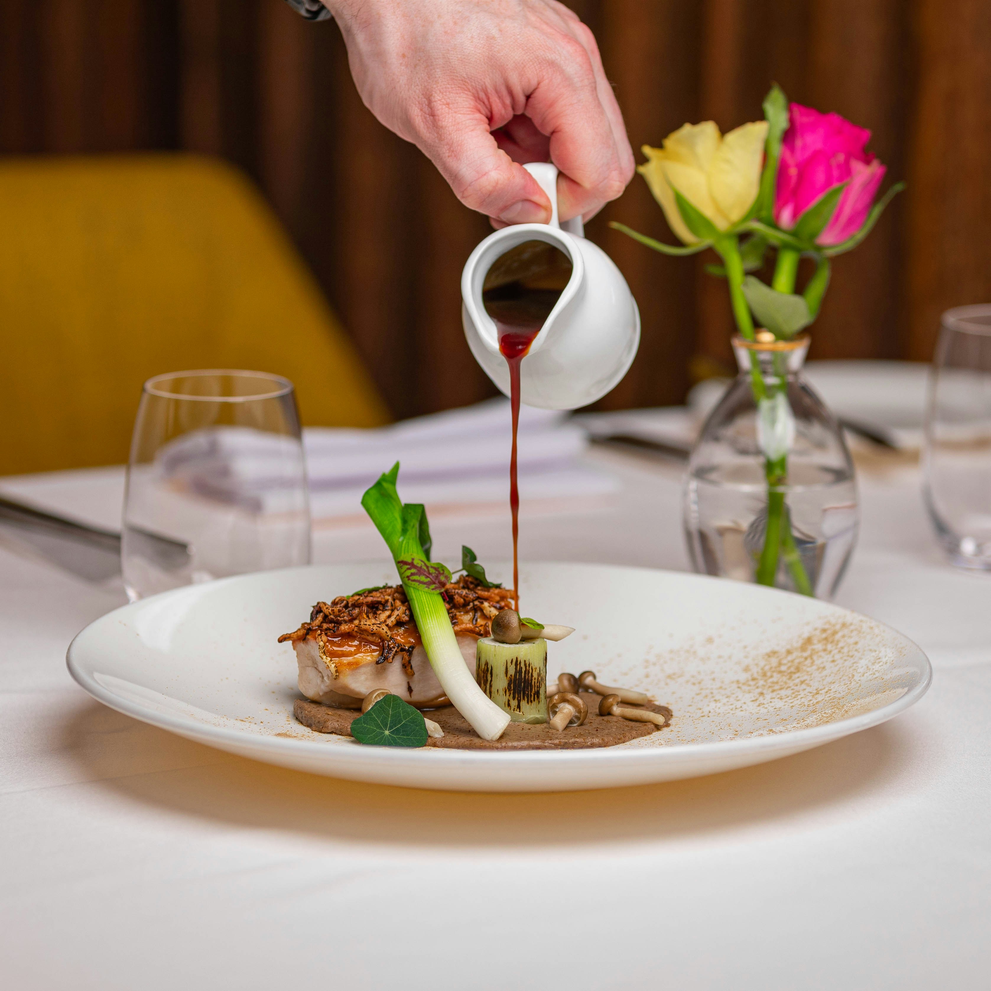 a person pouring sauce on a plate of food