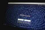 A website homepage displayed on a computer screen featuring a design made up of various letters and symbols, forming an artistic pattern around the central text that reads 'Midjourney'. Below the text, there are navigational options such as 'Join the Beta', 'Sign In', 'Getting Started', and 'Community Showcase'. The background is predominantly dark with white text.