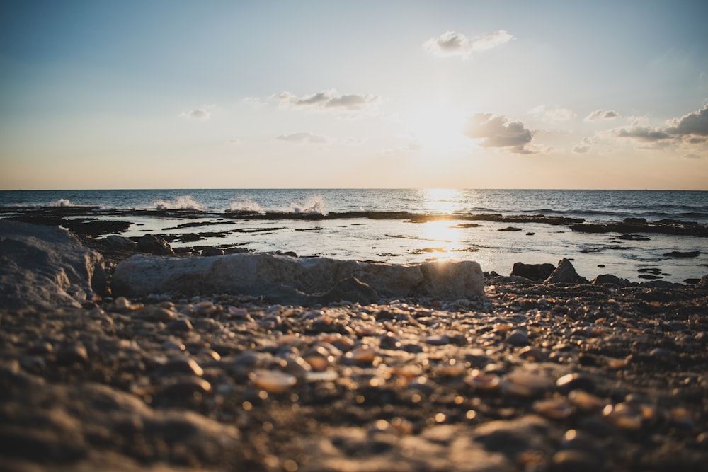 the sun is setting over the ocean and rocks