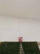 A no-smoking sign is mounted above a section of wall covered in artificial green grass. There are decorative lights arranged in a triangular pattern hanging down from the sign.