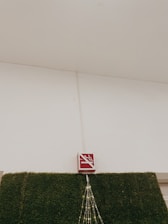 A no-smoking sign is mounted above a section of wall covered in artificial green grass. There are decorative lights arranged in a triangular pattern hanging down from the sign.