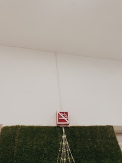 A no-smoking sign is mounted above a section of wall covered in artificial green grass. There are decorative lights arranged in a triangular pattern hanging down from the sign.