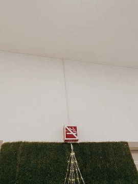 A no-smoking sign is mounted above a section of wall covered in artificial green grass. There are decorative lights arranged in a triangular pattern hanging down from the sign.