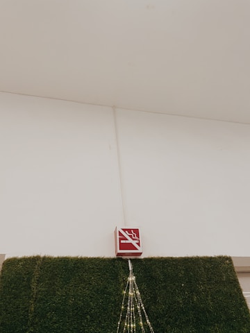 A no-smoking sign is mounted above a section of wall covered in artificial green grass. There are decorative lights arranged in a triangular pattern hanging down from the sign.